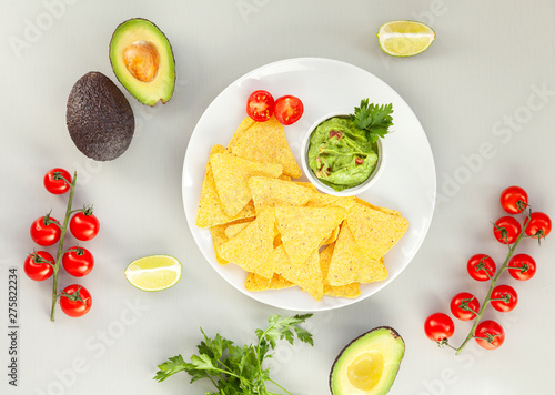 A delicious Bowl of Guacamole next to fresh ingredients on a table with tortilla chips. Traditional latin american mexican sauce guacamole on grey background. Top view.