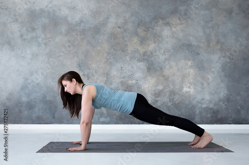 Young woman practicing yoga, doing Push ups or press ups exercise, phalankasana, Plank pose. Indoor full length