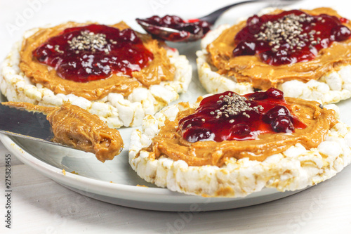 crunchy natural peanut butter strawberry jam jelly sandwich with chia seeds on rice cake bread. Proper nutrition diet vegetarian breakfast on plate next to knife with peanut butter