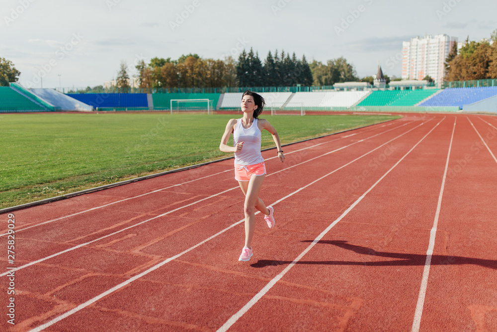 Young woman in pink shorts and tank to running during sunny morning on stadium track
