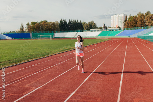 Athletic young woman in sportswear sprinting on running track stadium at sunset