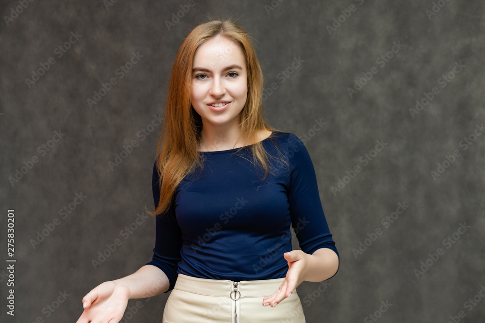 Portrait of a knee-high beautiful pretty red-haired woman girl in a blue jacket with a light skirt on a gray background in the studio. Smiles, shows emotions, talks, spreads his hands. Portrait of a knee-high beautiful pretty red-haired woman girl in a blue jacket with a light skirt on a gray background in the studio. Smiles, shows emotions, talks, spreads his hands.