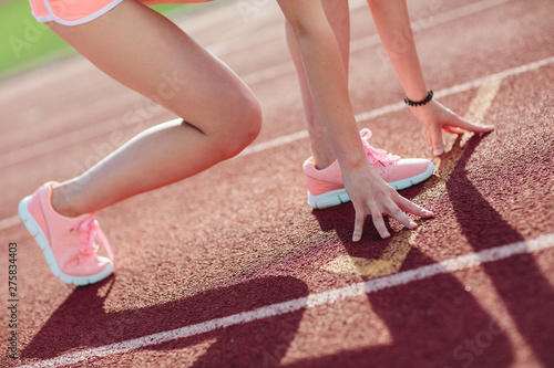 side view Athletic woman in pink shorts and tank tops on running track getting ready to start run, Amateur athlete. Close-up legs and arms