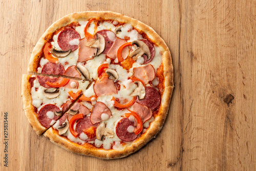 Top view of delicious Capricciosa Pizza on wooden table. Ingredients peeled tomato, cheese, ham, mushrooms, salami.