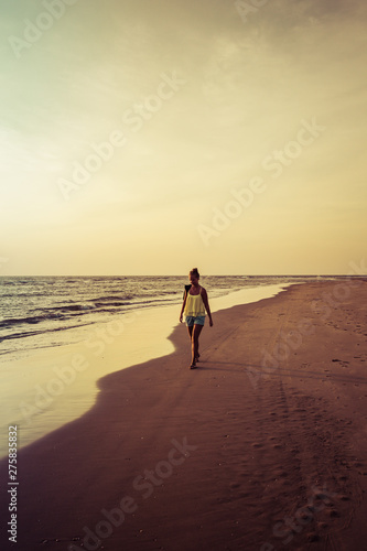 Girl walking along the beach at sunset