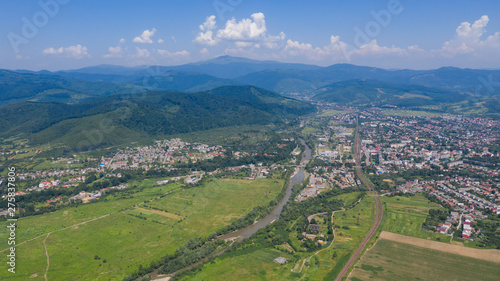 Aerial view of the Svalyava in Carpathian mountains. Natural background with geometric pattern - beige and red rectangles of the fields and roofs and lines of roads and trees. Zakarpattia, Ukraine.