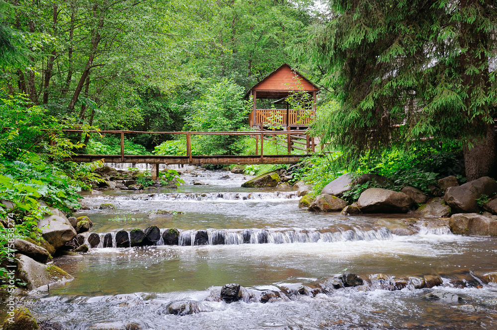 Mountain river, lush vegetation and recreation area with a bridge and gazebo.