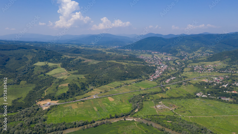 Aerial view of the Carpathian mountains. Natural background with geometric pattern - beige and red rectangles of the fields and roofs and lines of roads and trees. Zakarpattia, Ukraine.