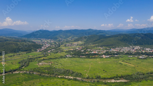 Aerial view of the Svalyava in Carpathian mountains. Natural background with geometric pattern - beige and red rectangles of the fields and roofs and lines of roads and trees. Zakarpattia, Ukraine.