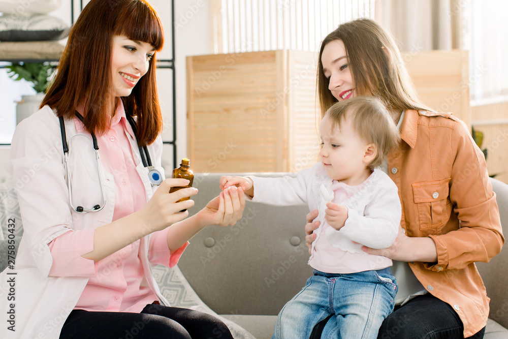 Obraz premium Young woman pediatrician prescribes and gives a medicine to ill baby girl, sitting with her mother