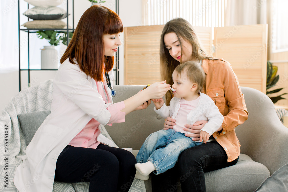 Woman doctor giving spoon dose of medicine liquid drinking syrup to child baby girl her patient. Doctor visit at home Woman doctor giving spoon dose of medicine liquid drinking syrup to child baby girl her patient. Doctor visit at home