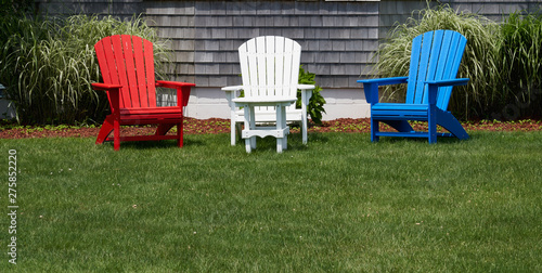 red white and blue wooden adirondack chairs on a green lawn in front of a house
