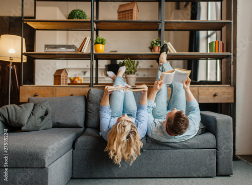 Couple with books lying on the couch upside down