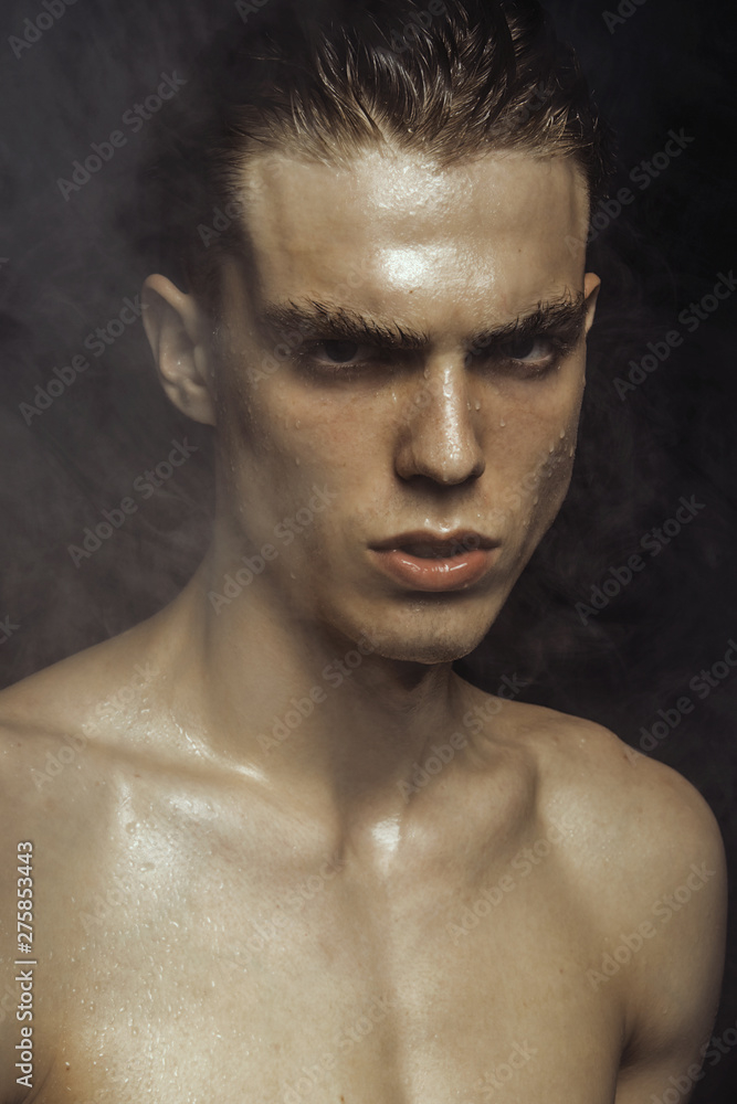 Handsome wet sport sexy stripped guy portrait with waterdrops and smoke on isolated black background