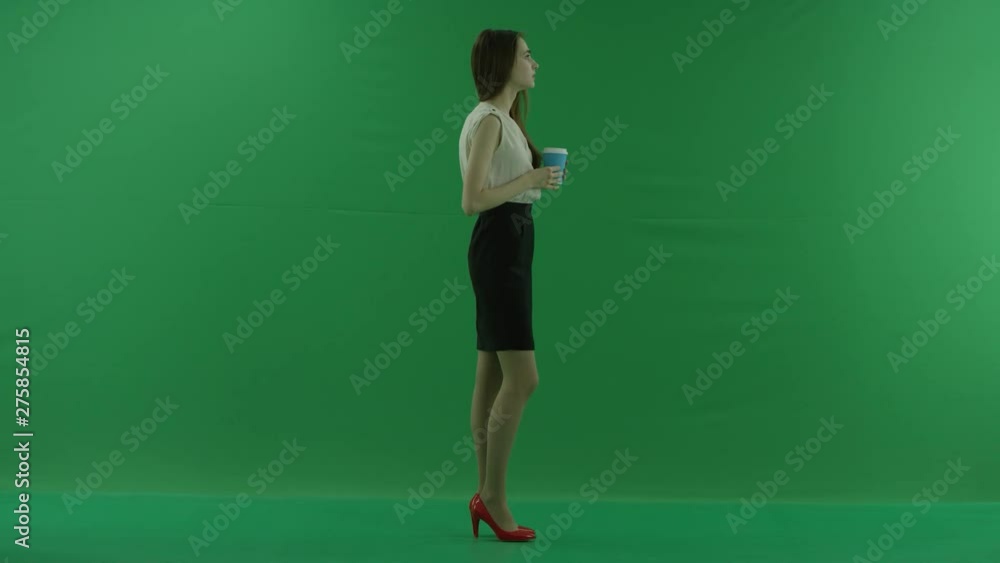 happy brunette young woman is holding a cup of coffee or tea and drinking. She stands sideways against green screen wearing formal clothes happy brunette young woman is holding a cup of coffee or tea and drinking. She stands sideways against green screen wearing formal clothes