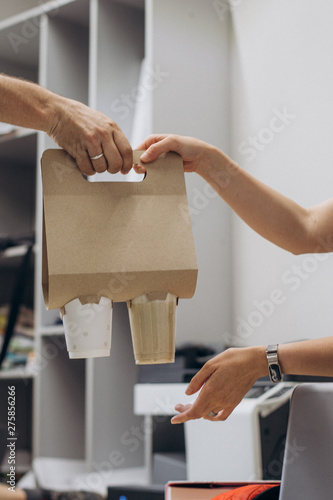 The hand of the courier is served by the owner with drinks for office workers who have ordered the delivery of coffee to the office. Coffee Take Away Order Online Delivery Concept photo