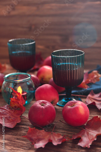 red apples  blue glasses with juice  maple leaves on wooden background