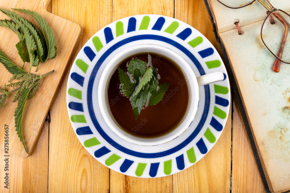 Tasty nettle tea in a cup. Freshly cut nettle and infected tea on a wooden table. Tasty nettle tea in a cup. Freshly cut nettle and infected tea on a wooden table.