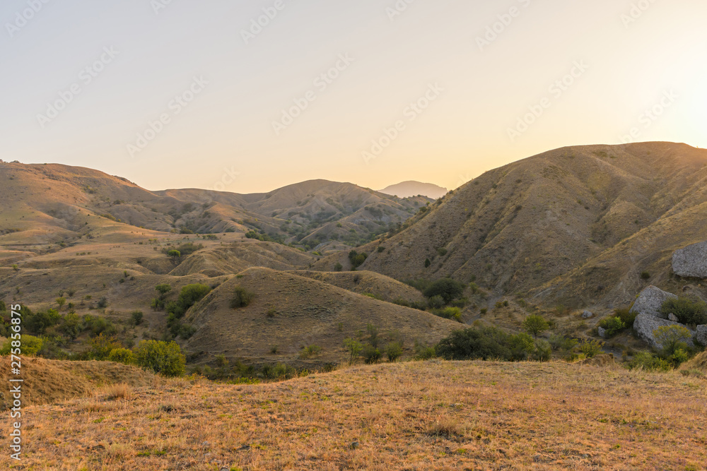 Fototapeta premium Hilly and mountainous steppe under the rays of the early sun with yellowed dry grass