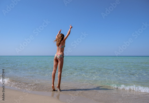 Slim and athletic girl in a colourful bikini on a wonderful beach with crystal clear water -vacation-fitness-wellness