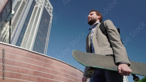 Young bearded male businessman ride on skateboard outdoors 