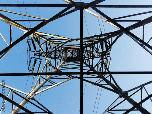 Low angle view of a high electricity pillar from inside against blue sky