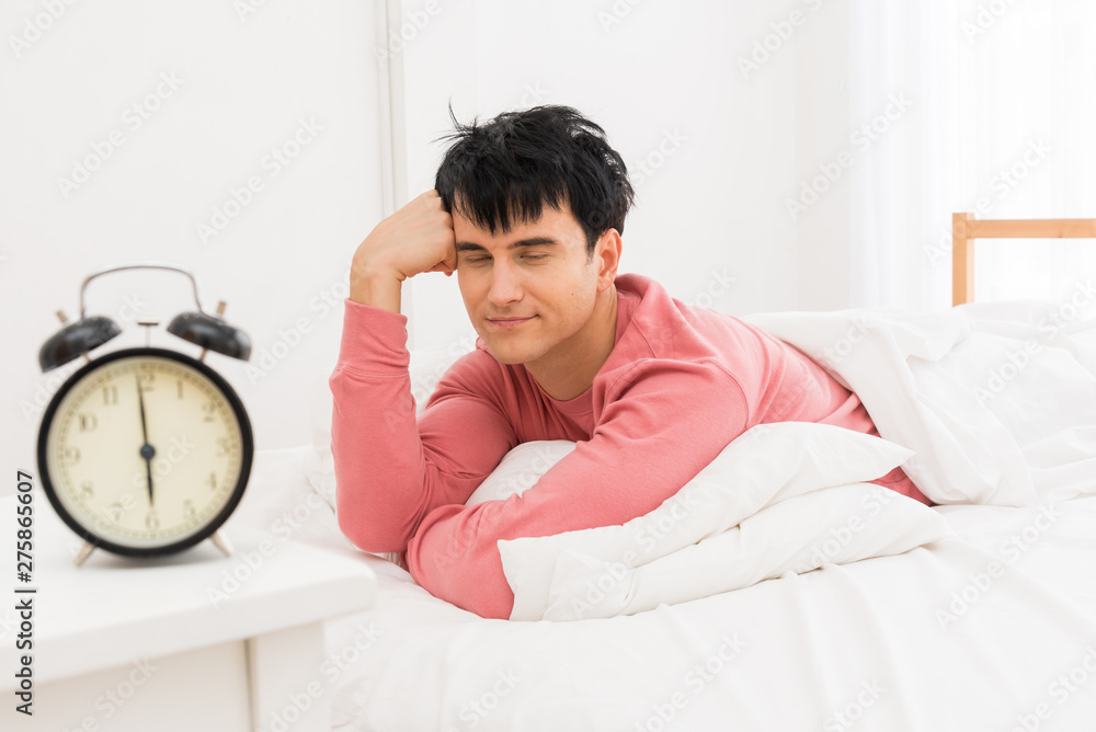 The young man was awakened by the morning alarm clock while on the bed.Shallow depth of field.unhappy from noisy sound of alarm clock and trying to turn it off. Hangover,lazy and sleepless concept. The young man was awakened by the morning alarm clock while on the bed.Shallow depth of field.unhappy from noisy sound of alarm clock and trying to turn it off. Hangover,lazy and sleepless concept.