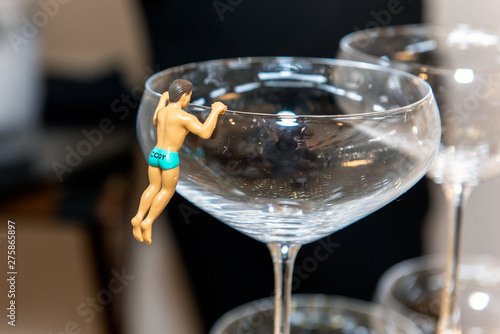 Champange glass decorated with male figurine clad in speedo swimsuit while climbing over rim. photo