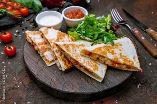 Quesadilla with chicken and sauces on dark board , on dark rustic concrete background