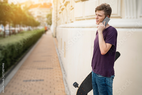 Millenial with long board talking on cell phone outdoors 