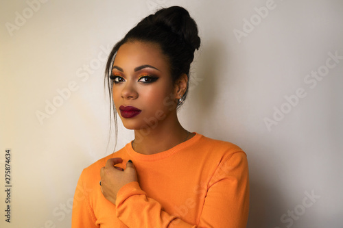 Portrait of attractive afro american young woman with fashion luxury makeup orange-coloured shades and her hair scraped back into high bun. Perfect Skin. Long eyelashes. Pouty lips. Beauty industry.
