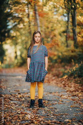 Autumn portrait of pretty young girl, kid model posing outdoor in forest, wearing plaid dress and yellow tights