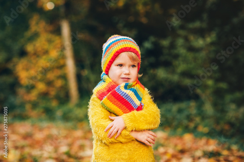 Outdoor portrait of cute toddler girl wearing yellow pullover  playing in autumn park