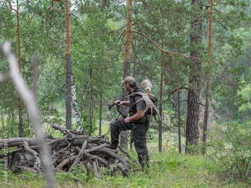 View of a hunter in the forest with a bow in the woods carries moose horns on his back