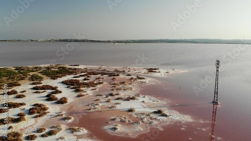 A panoramic aerial view high above the salt lake of Torrevieja in Spain. The lagoon is dyed red. In the background the salt mountains, the city and the deep blue Mediterranean sea.