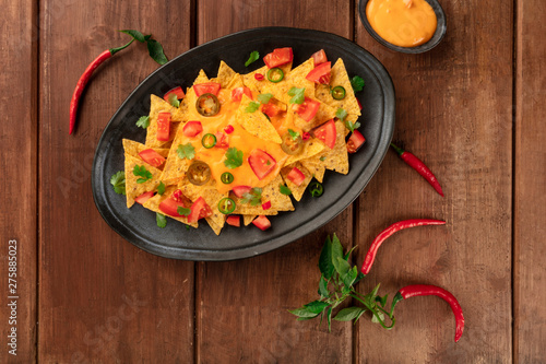 Nachos, Mexican tortilla chips, shot from the top with a cheese sauce, chili and jalapeno peppers, tomatoes. and cilantro, on a dark rustic wooden background with a place for text