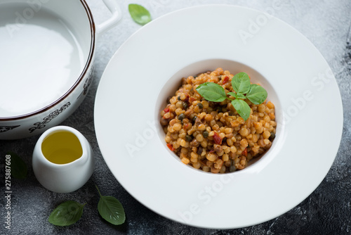 Italian fregola pasta served in a white plate with fresh green basil and olive oil, studio shot