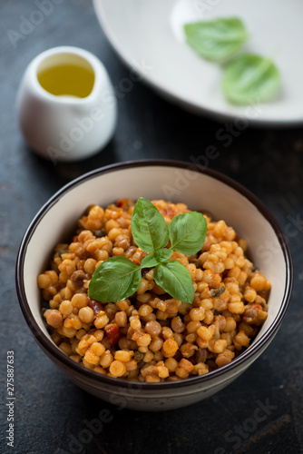 Bowl of fregola pasta with bell pepper and capers, vertical shot on a dark brown stone surface