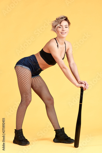 sexy slim cheerful smiling happy blonde model dancing with a bat  using it like a stick. full length photo. isolated yellow background