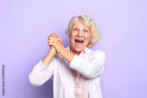 Valokuva Old blonde woman keeping hands, palms together , rejoicing at good news, winning of favourite team, light blue background