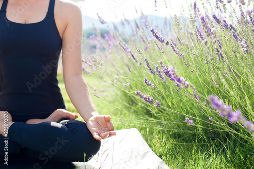 Fototapeta Naklejka Na Ścianę i Meble -  Woman is practicing yoga in lavender field. Girl is meditating, sitting in lotus pose outdoors. Sport workout at nature. Concept of healthy lifestyle, wellbeing. Female fitness classes. Close up