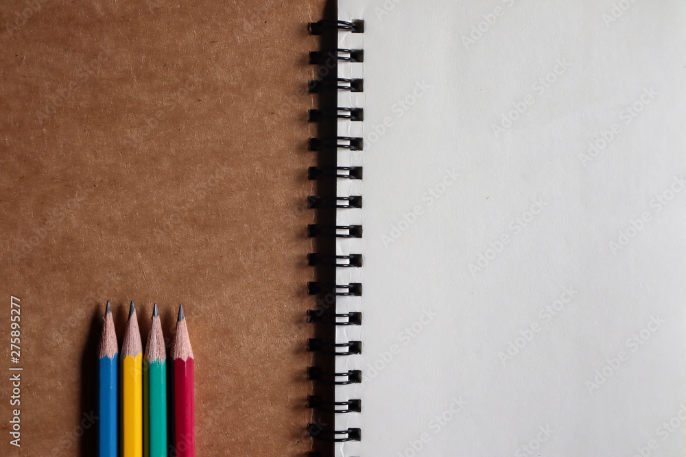 Multi-colored pencils with brown note book on brown paper background Multi-colored pencils with brown note book on brown paper background