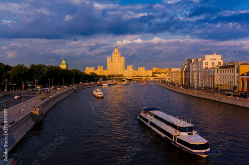 the ship sails on the river in the sunset light. a cityscape and a residential building with a spire on the background. Landscape of Moscow river
