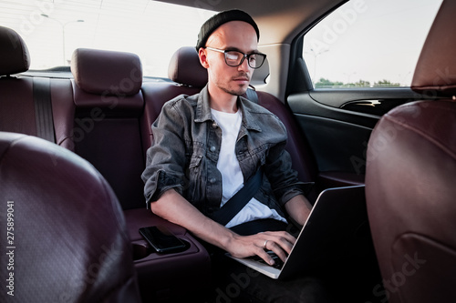 Young business person using laptop on a backseat of a car. Milennial person using modern technology while commuting by a private or rental car © Photoboyko