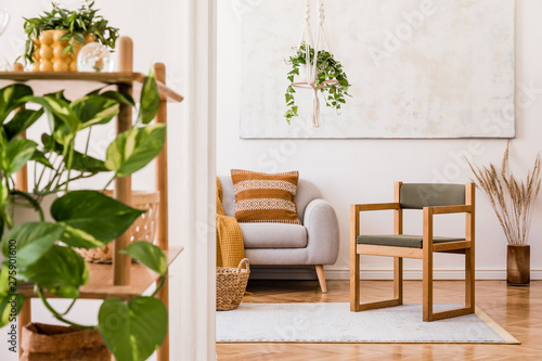 The stylish boho interior of living room in nice apartment with gray sofa, armchair, honey yellow plaid and pillows, plant and elegant accessories. Handmade macrame shelf planter hanger and paintings.