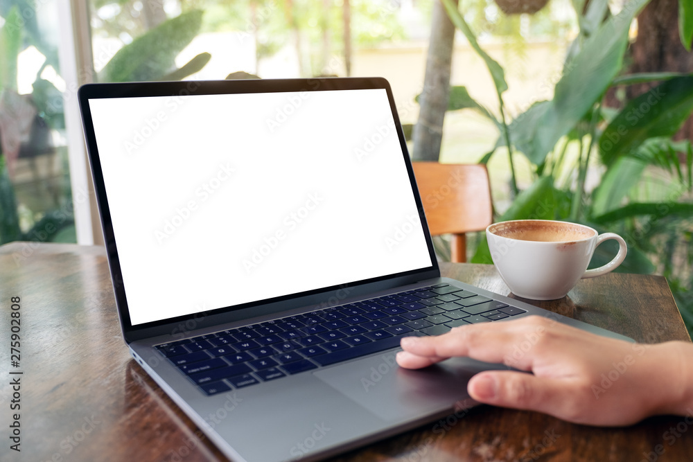 Mockup image of a woman using and touching laptop touchpad with blank white desktop screen while drinking coffee on wooden table Mockup image of a woman using and touching laptop touchpad with blank white desktop screen while drinking coffee on wooden table