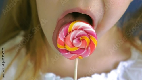 Little girl with a lollipop on a blue background. Close up portrait