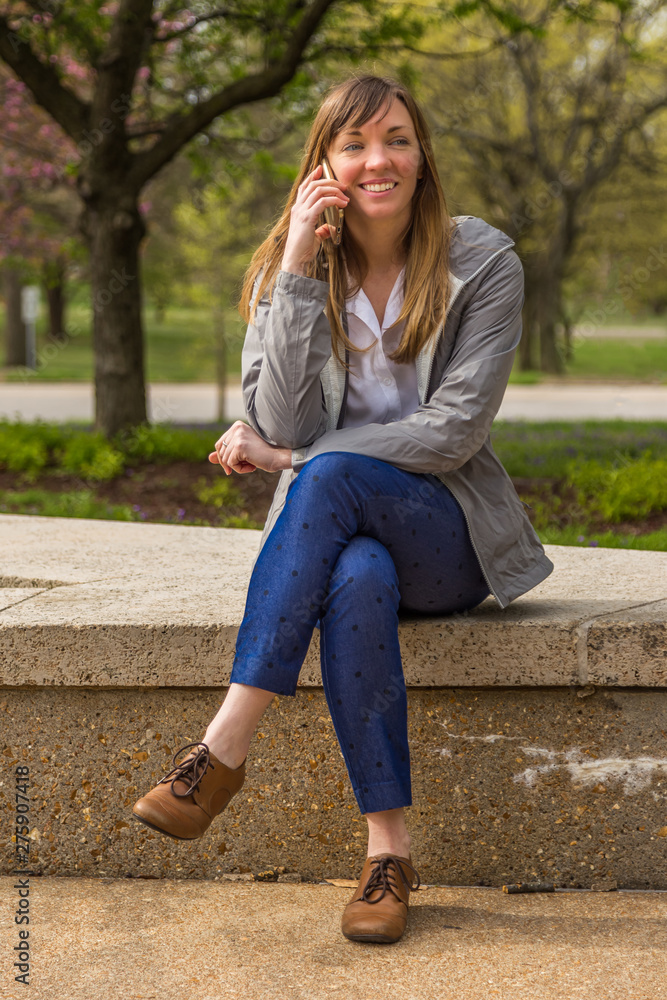 Young woman sitting in a park while talking on her phone. Young woman sitting in a park while talking on her phone.