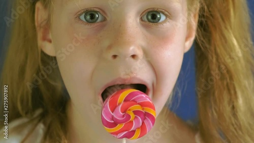 Little girl with a lollipop on a blue background. Close up portrait