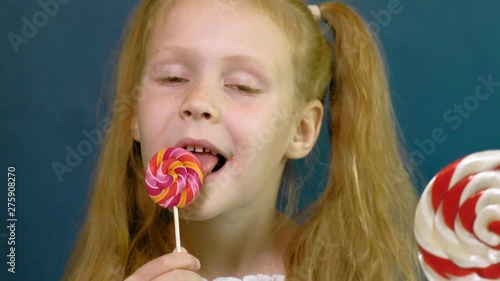 Little girl with a lollipop on a blue background. Close up portrait